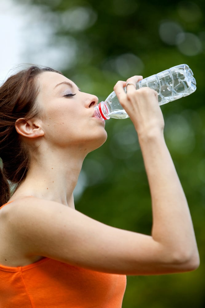 Fit woman in tracksuit drinking water outdoors